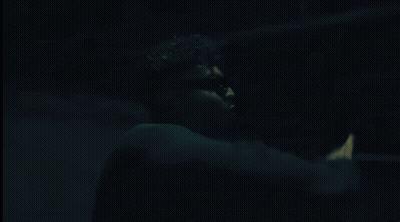 A Man Wearing Sunglasses And A Choker Is Standing In A Dark Room GIF