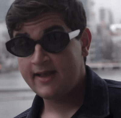 A Man Wearing Sunglasses And A Denim Jacket Looks At The Camera GIF