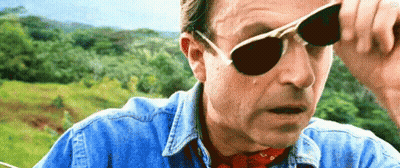 A Man Wearing Sunglasses And A Denim Shirt Is Looking At Something . GIF