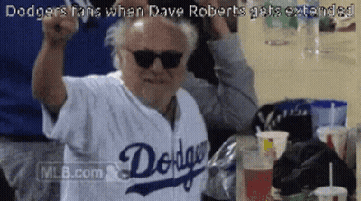 A Man Wearing Sunglasses And A Dodgers Jersey Holds His Fist Up In The Air GIF