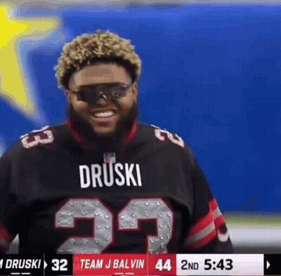 A Man Wearing Sunglasses And A Druski Jersey Is Smiling GIF
