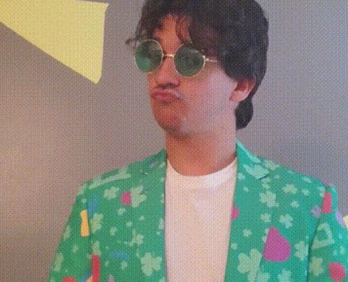 A Man Wearing Sunglasses And A Green Jacket Is Making A Face GIF