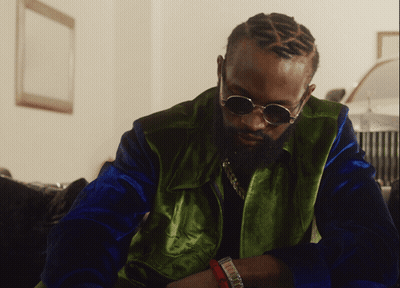 A Man Wearing Sunglasses And A Green Jacket Looks Down GIF