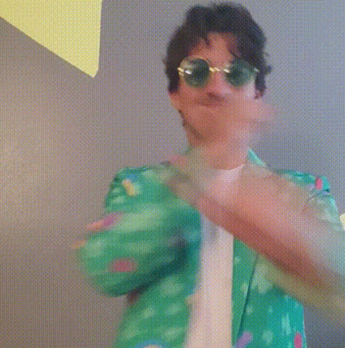 A Man Wearing Sunglasses And A Green Shirt Is Making A Heart With His Hands . GIF