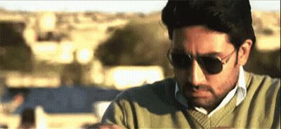 A Man Wearing Sunglasses And A Green Sweater Is Sitting On A Balcony . GIF