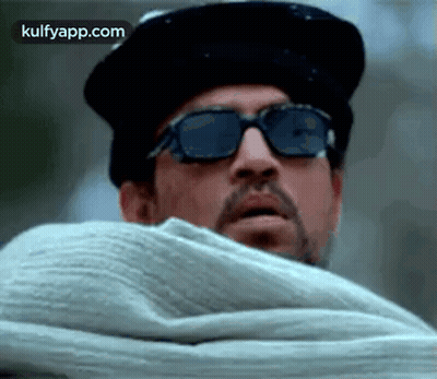 A Man Wearing Sunglasses And A Hat Is Covering His Face With A Blanket . GIF