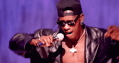 A Man Wearing Sunglasses And A Hat Is Singing Into A Microphone . GIF