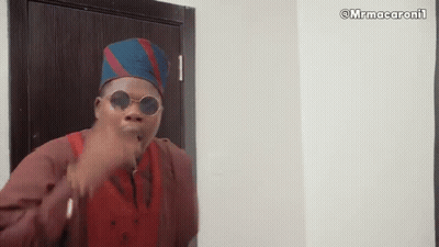 A Man Wearing Sunglasses And A Hat Is Standing In Front Of A Door And Making A Funny Face . GIF