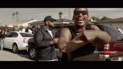 A Man Wearing Sunglasses And A Hat Is Standing In Front Of A Red Suv And A White Car . GIF