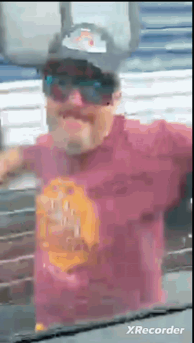 A Man Wearing Sunglasses And A Hat Is Standing In Front Of A Wall . GIF