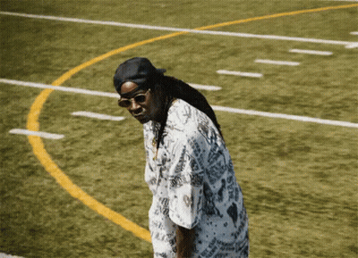 A Man Wearing Sunglasses And A Hat Is Standing On A Field GIF