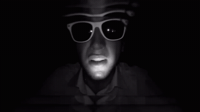 A Man Wearing Sunglasses And A Hat Looks At The Camera GIF
