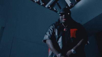 A Man Wearing Sunglasses And A Hat Stands In Front Of A Crowd Of People GIF