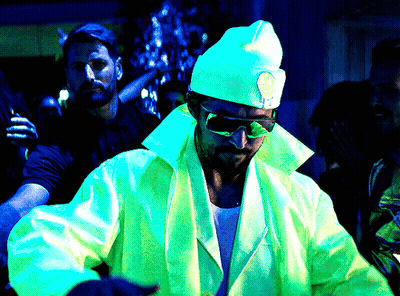 A Man Wearing Sunglasses And A Hat With A Smiley Face On It Stands In A Dark Room GIF