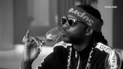 A Man Wearing Sunglasses And A Headband Is Drinking From A Wine Glass . GIF
