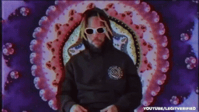 A Man Wearing Sunglasses And A Hoodie Is Standing In Front Of A Colorful Circle . GIF