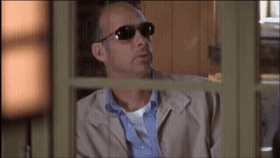 A Man Wearing Sunglasses And A Jacket Looks Out A Window GIF