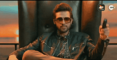 A Man Wearing Sunglasses And A Leather Jacket Is Sitting In A Chair Holding A Remote Control GIF