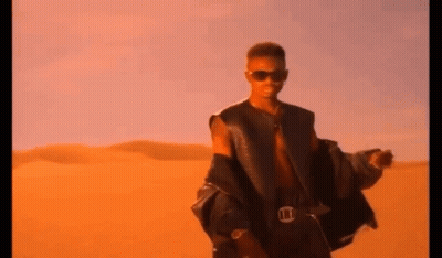 A Man Wearing Sunglasses And A Leather Jacket Is Standing In The Desert . GIF