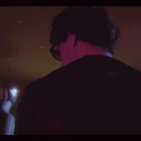 A Man Wearing Sunglasses And A Leather Jacket Looks At The Camera GIF
