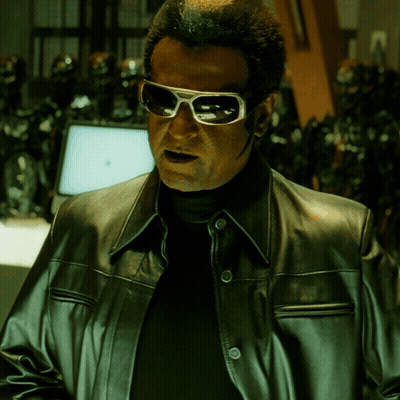 A Man Wearing Sunglasses And A Leather Jacket Stands In Front Of A Computer Monitor GIF