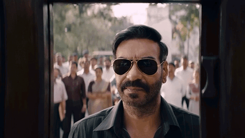 A Man Wearing Sunglasses And A Mustache Is Standing In Front Of A Crowd GIF
