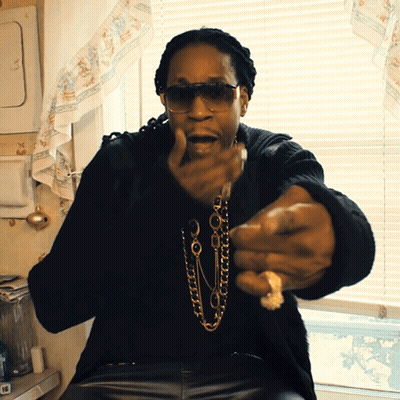 A Man Wearing Sunglasses And A Necklace Is Sitting In Front Of A Window In A Kitchen GIF