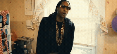 A Man Wearing Sunglasses And A Necklace Is Standing In A Room . GIF