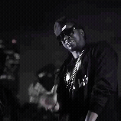 A Man Wearing Sunglasses And A Necklace Is Standing In The Dark . GIF
