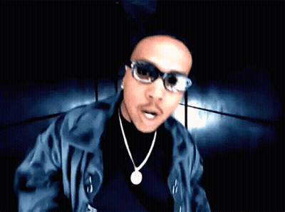 A Man Wearing Sunglasses And A Necklace Looks At The Camera With His Mouth Open GIF