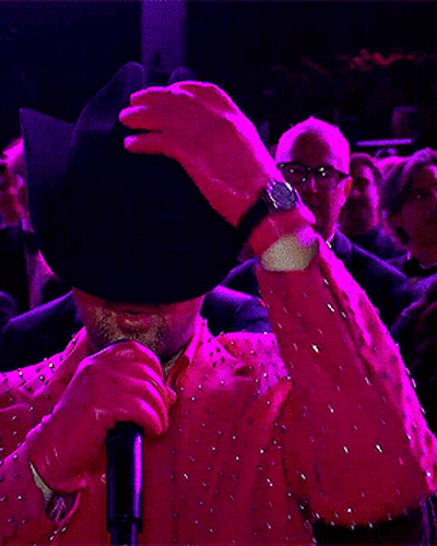 A Man Wearing Sunglasses And A Pink Jacket Is Holding A Microphone GIF