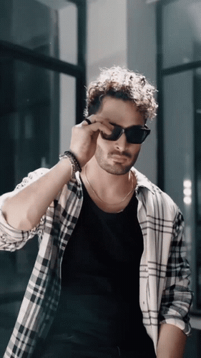 A Man Wearing Sunglasses And A Plaid Shirt Adjusts His Sunglasses GIF