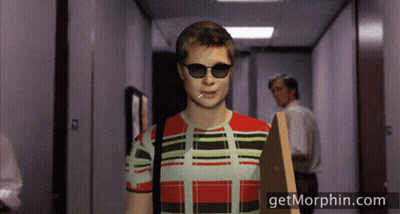 A Man Wearing Sunglasses And A Plaid Shirt Is Walking Down A Hallway With Getmorphin.com On The Bottom GIF