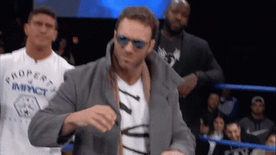 A Man Wearing Sunglasses And A Property Of Impact Shirt Stands In A Boxing Ring GIF