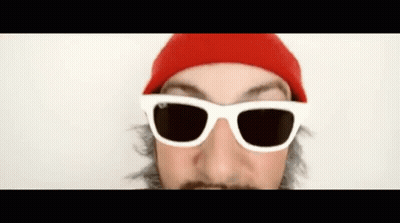 A Man Wearing Sunglasses And A Red Hat Looks At The Camera GIF