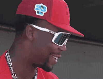 A Man Wearing Sunglasses And A Red Hat Smiles GIF