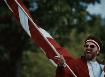 A Man Wearing Sunglasses And A Red Jacket Is Holding A Red And White Flag GIF