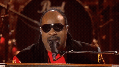 A Man Wearing Sunglasses And A Red Shirt Is Singing Into A Microphone In Front Of A Drum Set With The Letter D On It GIF