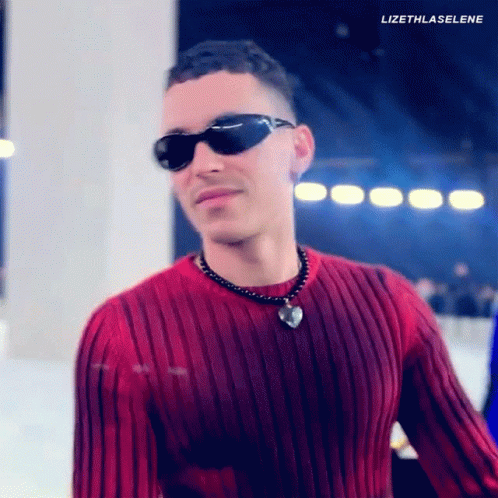 A Man Wearing Sunglasses And A Red Sweater Has A Heart Necklace Around His Neck . GIF