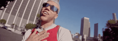 A Man Wearing Sunglasses And A Red Vest Is Standing In Front Of A City Skyline GIF