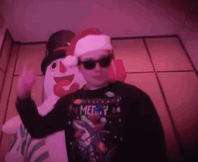 A Man Wearing Sunglasses And A Santa Hat Is Standing In Front Of A Snowman . GIF