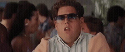 A Man Wearing Sunglasses And A Striped Shirt Is Standing In A Crowd . GIF