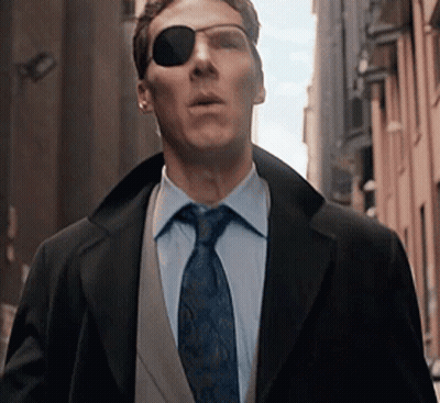 A Man Wearing Sunglasses And A Suit And Tie Is Walking Down A City Street . GIF