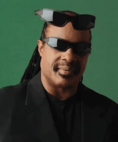 A Man Wearing Sunglasses And A Suit Is Smiling . GIF