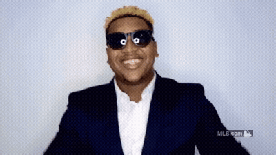 A Man Wearing Sunglasses And A Suit Is Smiling In Front Of A Mlb Logo GIF