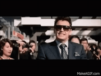 A Man Wearing Sunglasses And A Suit Is Standing In Front Of A Crowd Of People . GIF
