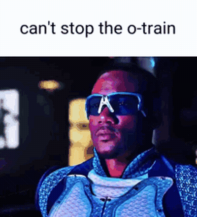 A Man Wearing Sunglasses And A Suit Is Standing In Front Of A Sign That Says Can 'T Stop The O-Train GIF