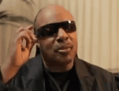 A Man Wearing Sunglasses And A Suit Is Talking On A Cell Phone . GIF