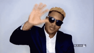 A Man Wearing Sunglasses And A Suit Is Waving His Hand GIF
