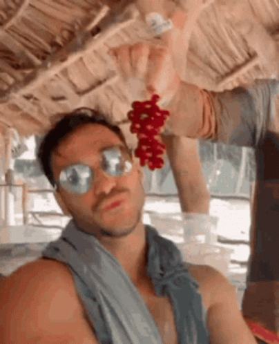 A Man Wearing Sunglasses And A Towel Is Holding A Bunch Of Grapes GIF